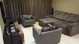 O living com sofá retrátil e duas poltronas giratórias, recebeu tecidos em tons de cinza e a cortina escura deixa o ambiente elegante.